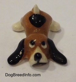 A brown with white and black Hound Dawg figurine is laying down and it has a black spot near its tail.